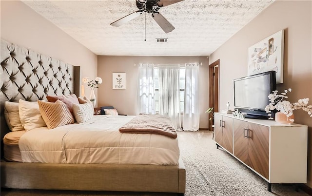 bedroom featuring a textured ceiling, light colored carpet, and ceiling fan