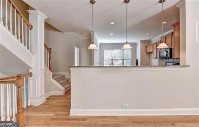 kitchen featuring light wood finished floors, baseboards, hanging light fixtures, crown molding, and black microwave