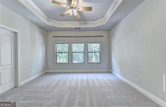 carpeted spare room with a raised ceiling, crown molding, and baseboards