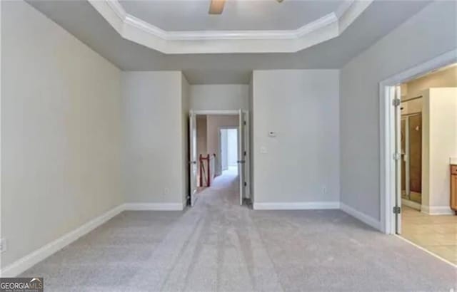 unfurnished bedroom featuring baseboards, ornamental molding, a raised ceiling, and light colored carpet