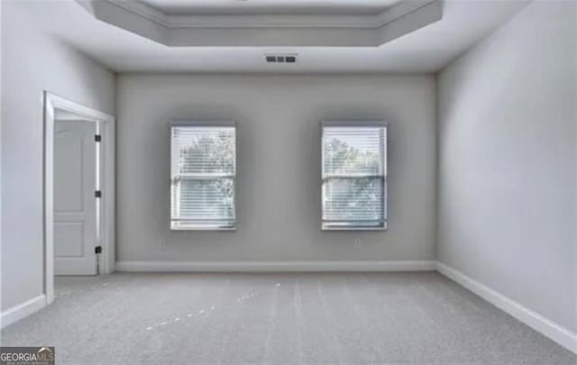 carpeted empty room featuring a tray ceiling, visible vents, and baseboards