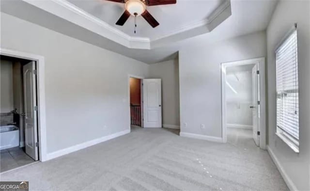 unfurnished bedroom with carpet floors, a raised ceiling, ornamental molding, ensuite bath, and baseboards