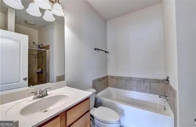 bathroom featuring visible vents, toilet, vanity, a bath, and walk in shower