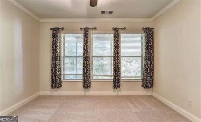 empty room featuring light carpet, baseboards, visible vents, ceiling fan, and crown molding