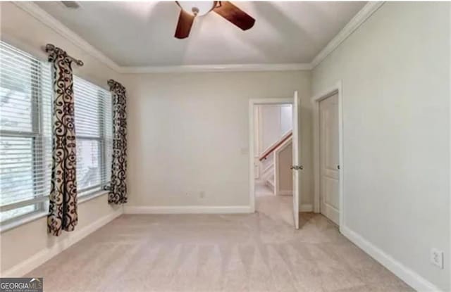 spare room featuring light carpet, ceiling fan, ornamental molding, and baseboards