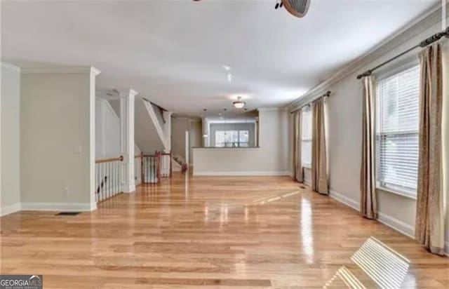 unfurnished living room with light wood finished floors, ornamental molding, and baseboards