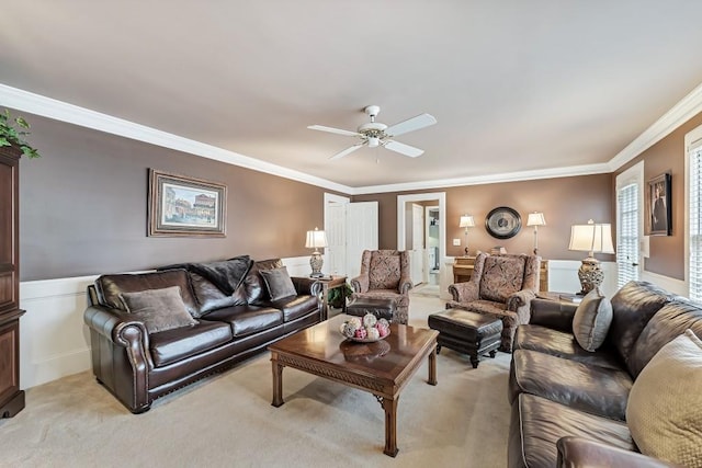 living area with ornamental molding, a ceiling fan, wainscoting, and light carpet