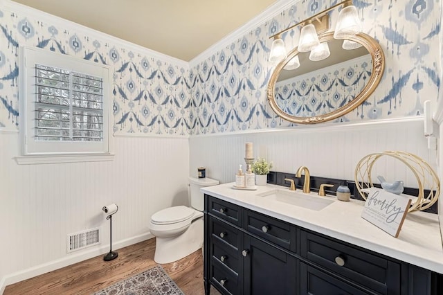 bathroom featuring a wainscoted wall, wallpapered walls, visible vents, and wood finished floors