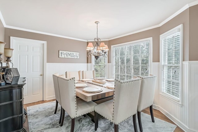 dining area featuring a chandelier, wainscoting, crown molding, and light wood-type flooring