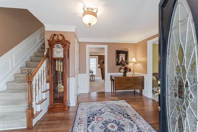 foyer with a wainscoted wall, wood finished floors, stairway, crown molding, and a decorative wall