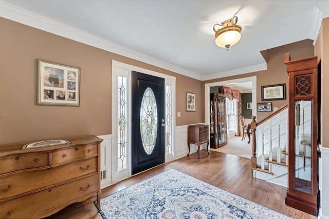 entrance foyer with stairs, crown molding, wood finished floors, and a wainscoted wall