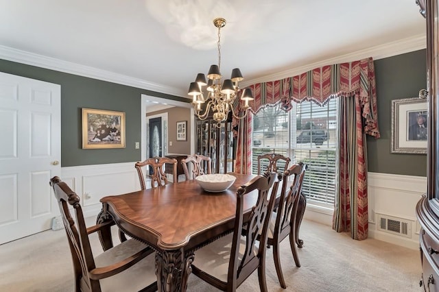 dining space featuring visible vents, ornamental molding, an inviting chandelier, wainscoting, and light colored carpet