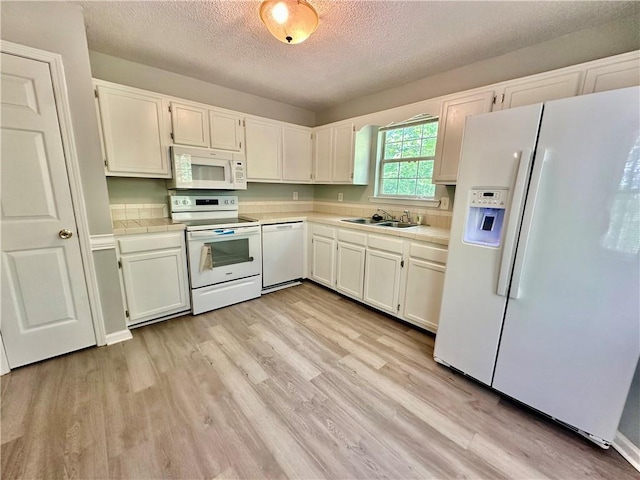 kitchen featuring white appliances, a textured ceiling, tile counters, and a sink