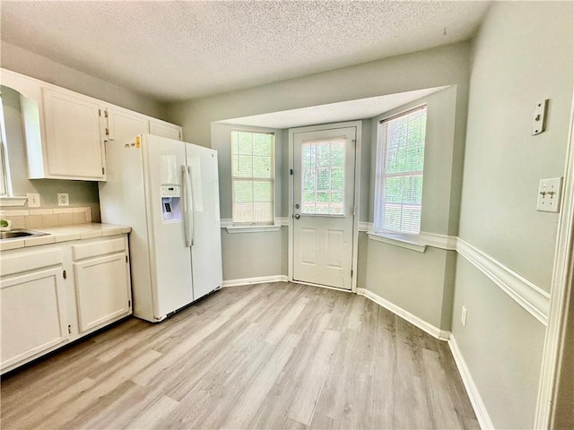 kitchen with white cabinets, light wood-type flooring, tile counters, and white refrigerator with ice dispenser
