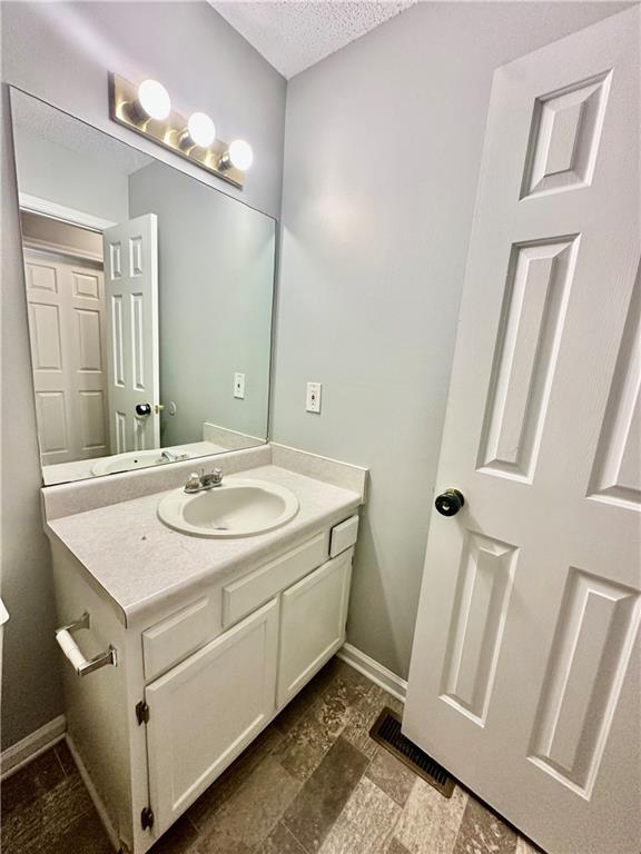 bathroom with baseboards, visible vents, a textured ceiling, and vanity