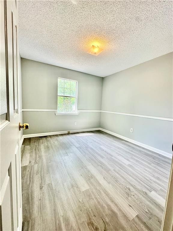 spare room with a textured ceiling, wood finished floors, and baseboards
