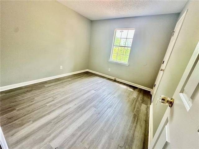 spare room with a textured ceiling, wood finished floors, and baseboards
