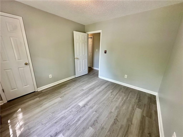 unfurnished bedroom with a textured ceiling, wood finished floors, and baseboards