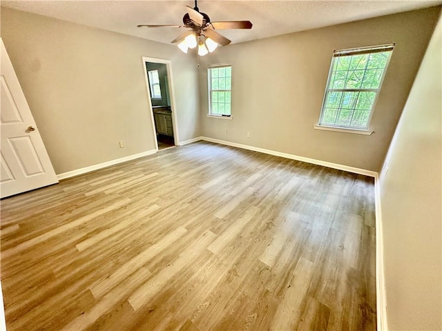unfurnished bedroom featuring ceiling fan, ensuite bath, baseboards, a textured ceiling, and wood finished floors