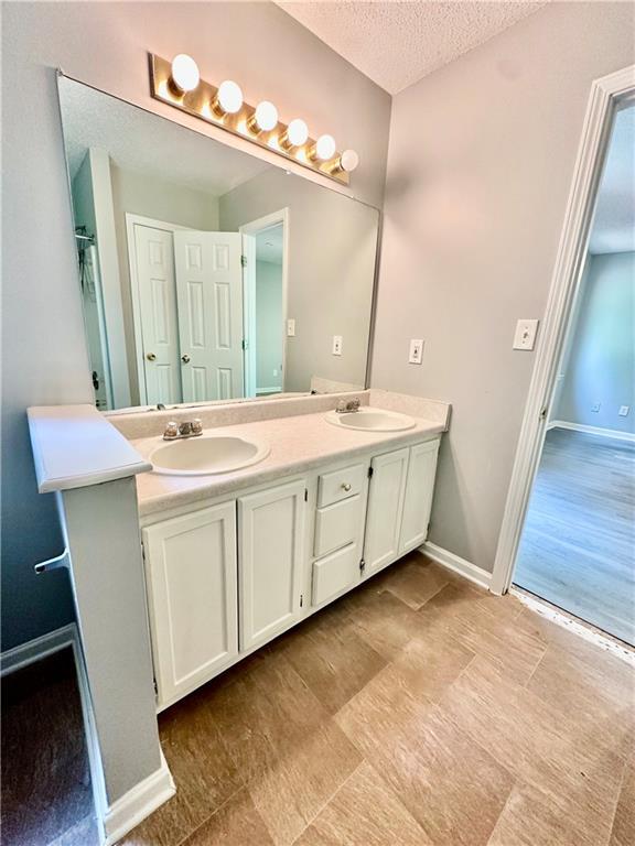 full bathroom with baseboards, a textured ceiling, double vanity, and a sink