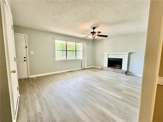 unfurnished living room featuring a fireplace with raised hearth, ceiling fan, baseboards, a textured ceiling, and wood finished floors