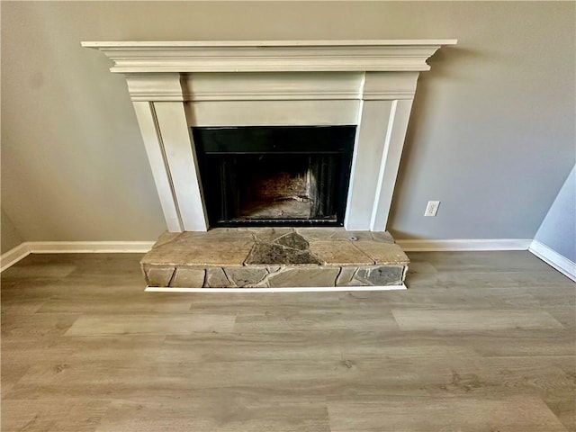interior details featuring baseboards, wood finished floors, and a fireplace with raised hearth
