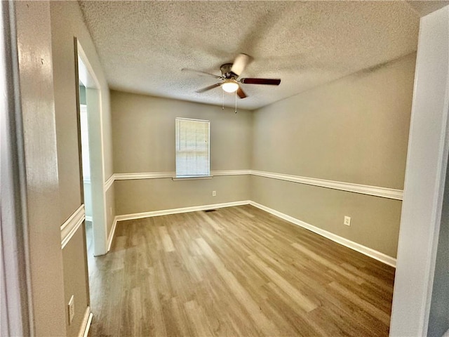 unfurnished room featuring wood finished floors, ceiling fan, baseboards, and a textured ceiling