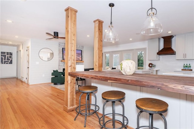 kitchen featuring wooden counters, tasteful backsplash, custom exhaust hood, white cabinetry, and hanging light fixtures