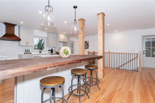 kitchen with hanging light fixtures, wooden counters, decorative backsplash, white cabinets, and custom exhaust hood