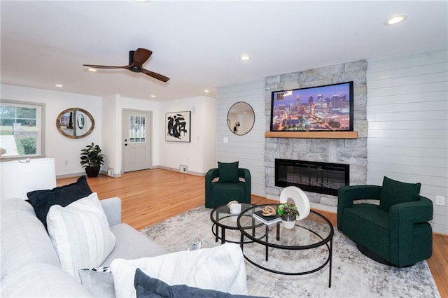 living room featuring ceiling fan, a large fireplace, and wood-type flooring