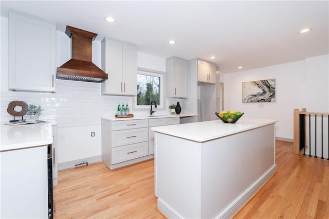 kitchen featuring custom exhaust hood, backsplash, white cabinets, light hardwood / wood-style flooring, and a kitchen island