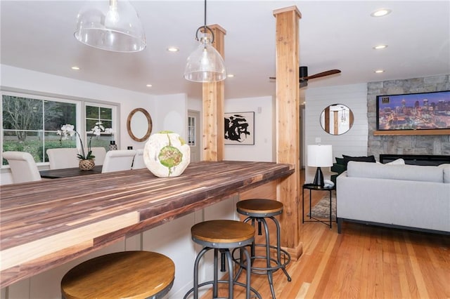 kitchen with a stone fireplace, wood walls, decorative light fixtures, a kitchen bar, and light wood-type flooring