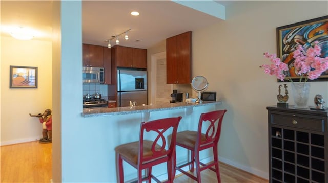 3338 Peachtree Rd NE Unit 1506, Atlanta, GA 30326 - kitchen with appliances with stainless steel finishes, wood finished floors, baseboards, a breakfast bar area, and brown cabinetry