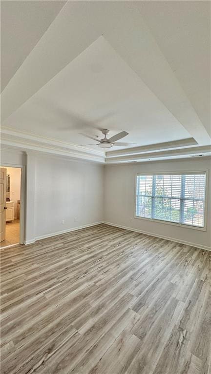 spare room featuring a ceiling fan, a raised ceiling, light wood-style flooring, and baseboards