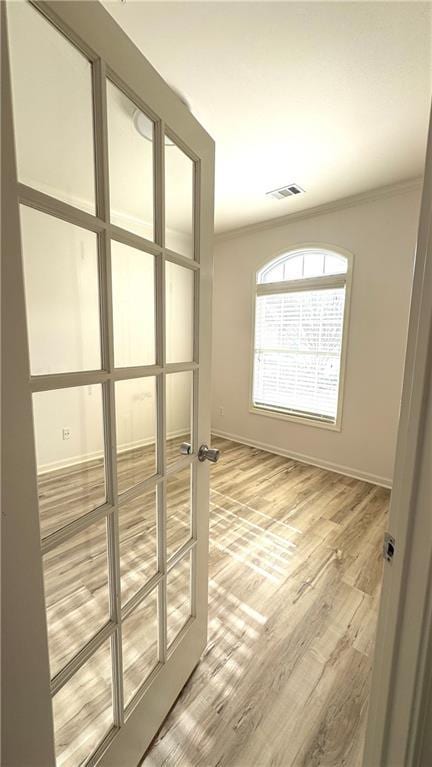 interior space featuring baseboards, visible vents, crown molding, and light wood finished floors