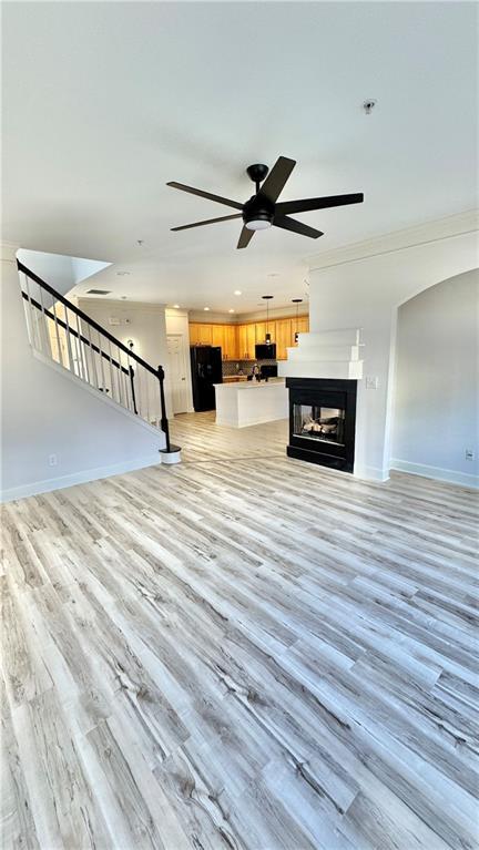 unfurnished living room with light wood-style floors, baseboards, a multi sided fireplace, and stairs