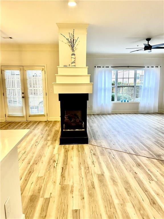 unfurnished living room featuring ceiling fan, a fireplace, crown molding, and wood finished floors