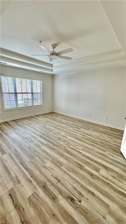 spare room featuring a raised ceiling, ceiling fan, light wood-style flooring, and baseboards