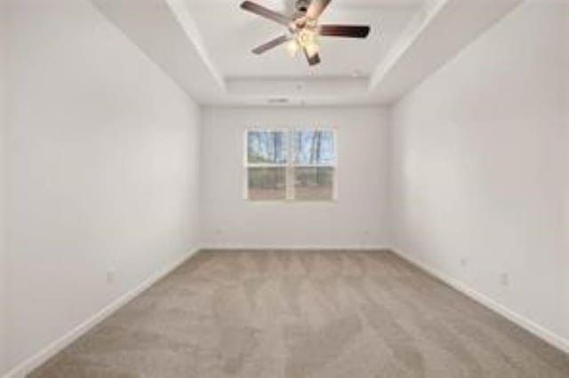 carpeted empty room featuring baseboards, ceiling fan, and a tray ceiling
