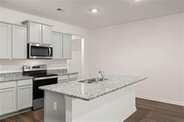kitchen with appliances with stainless steel finishes, dark wood finished floors, a sink, light stone counters, and an island with sink