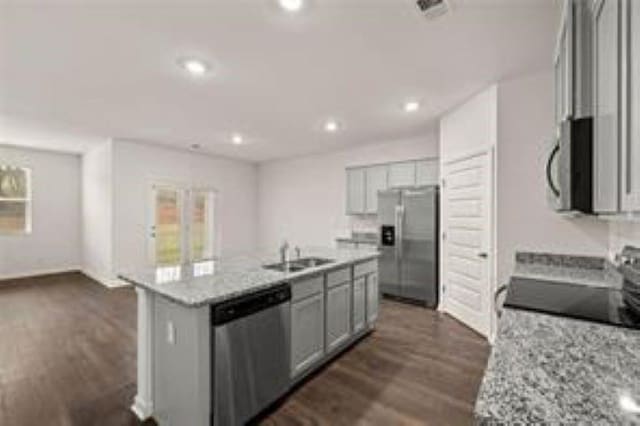 kitchen featuring an island with sink, a sink, gray cabinetry, stainless steel appliances, and dark wood-type flooring