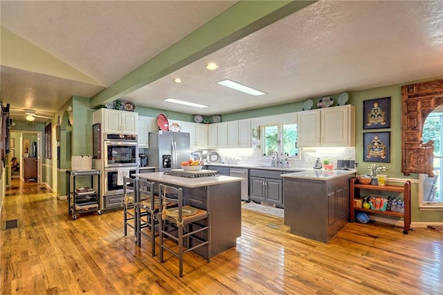 476 Franklin St, Dillard, GA 30537 - kitchen with stainless steel appliances, a textured ceiling, a kitchen bar, light wood-type flooring, and white cabinetry