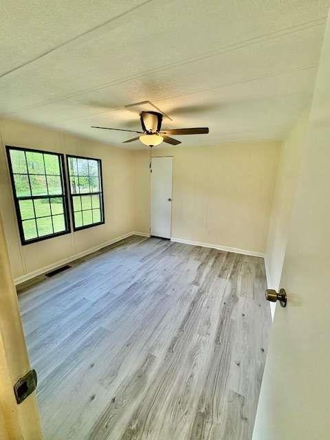 unfurnished room with wood finished floors, ceiling fan, visible vents, and baseboards