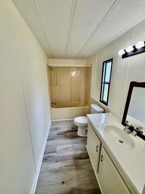 bathroom with wood finished floors, bathing tub / shower combination, toilet, vanity, and a textured ceiling