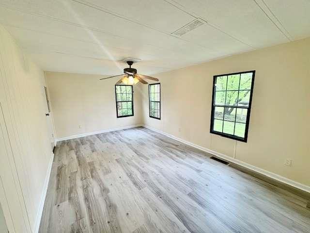 spare room with a ceiling fan, visible vents, wood finished floors, and baseboards