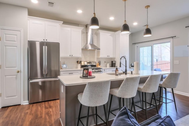 kitchen featuring white cabinetry, appliances with stainless steel finishes, pendant lighting, and wall chimney exhaust hood