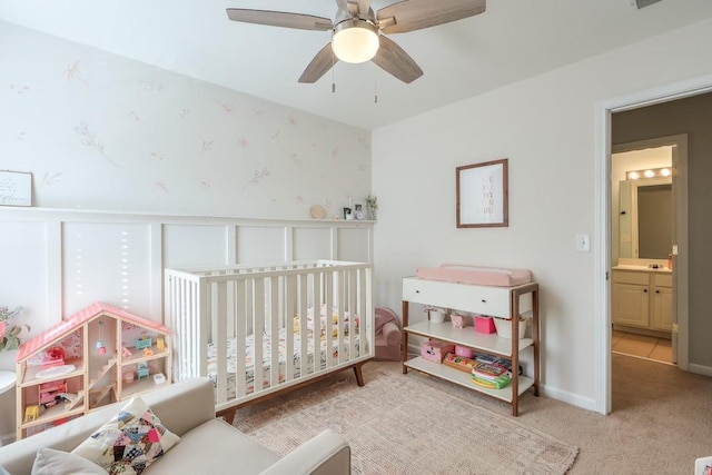 bedroom with a crib, light colored carpet, and ceiling fan