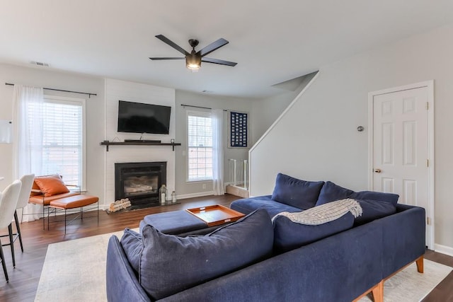 living room featuring dark wood-type flooring, a large fireplace, and ceiling fan