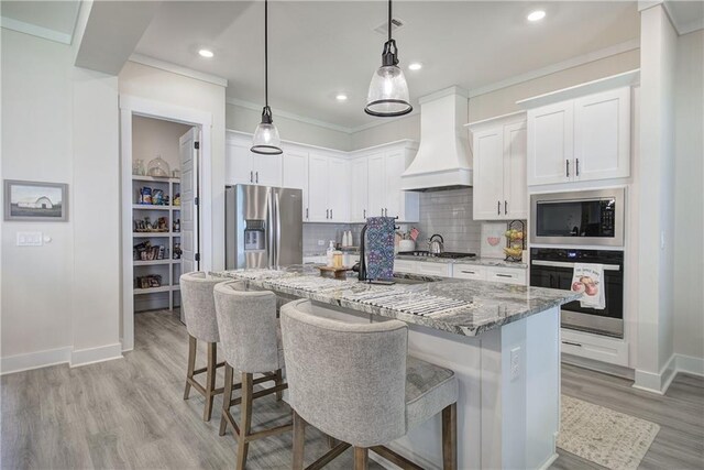 884 Oxford Rd, Ball Ground, GA 30107 - kitchen featuring stainless steel appliances, premium range hood, light stone counters, light wood-type flooring, and a breakfast bar area