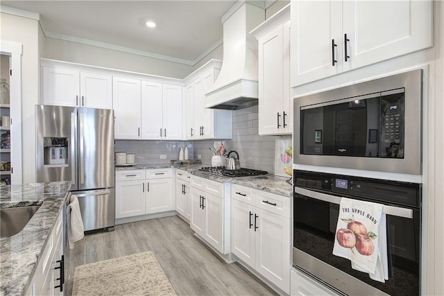 884 Oxford Rd, Ball Ground, GA 30107 - kitchen featuring appliances with stainless steel finishes, premium range hood, white cabinetry, ornamental molding, and light wood finished floors